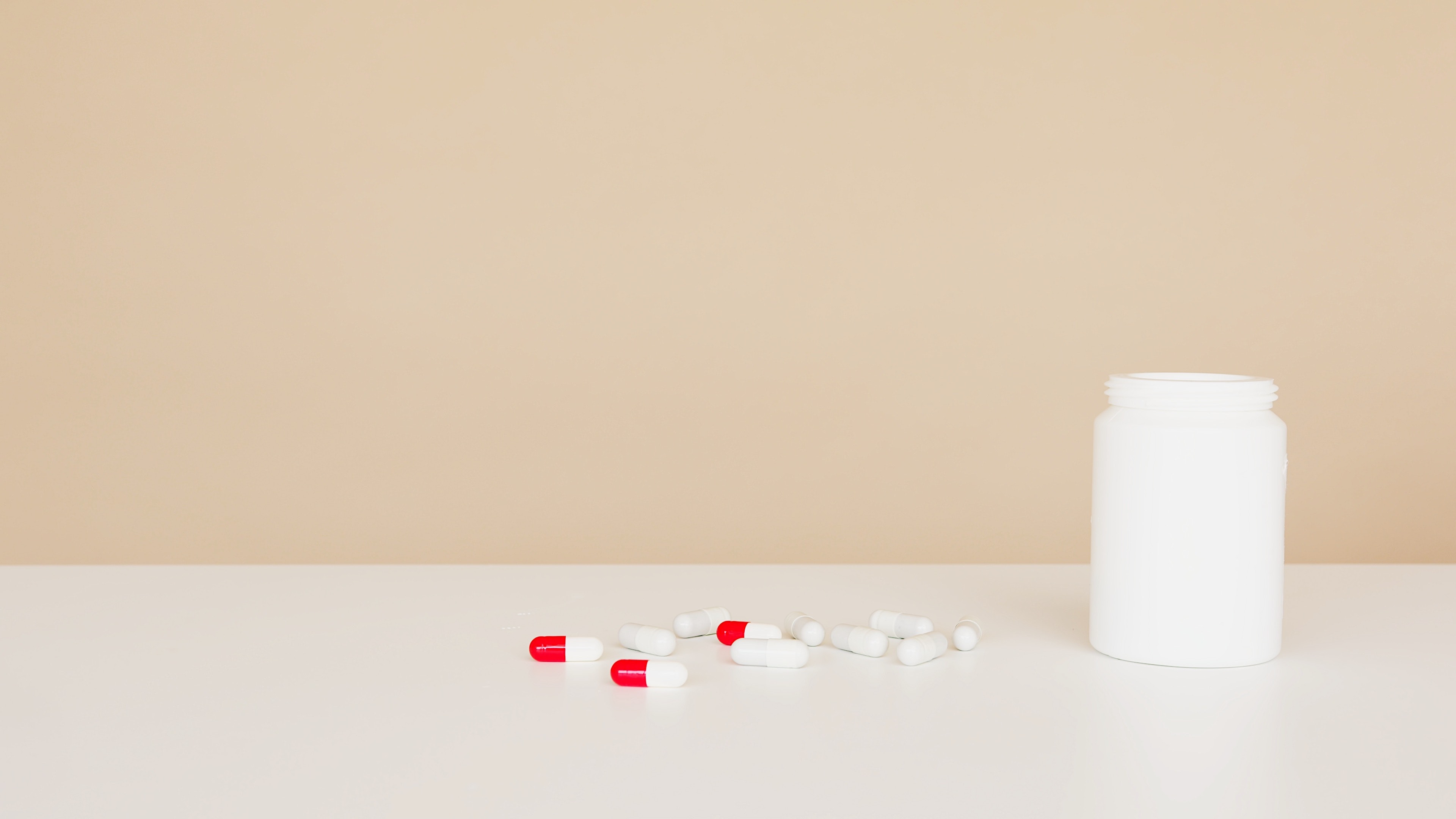 Nondescript white pill bottle and white and red pills on a white counter 
