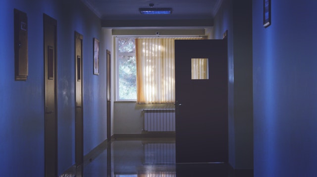 Hospital room at the end of a dark hallway lit by sunlight