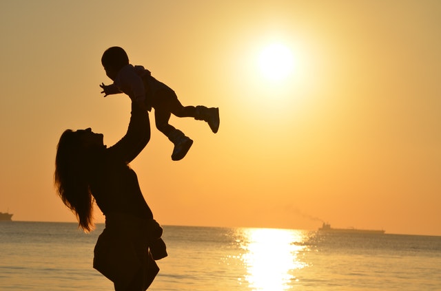 Mother holds child above her head as the sun sets on the beach