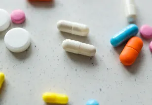 Assortment of white and brightly colored pills of different shapes and sizes scattered on a white tabletop