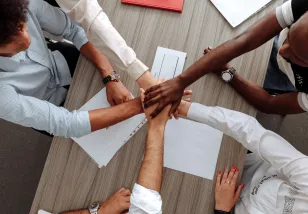 Aerial picture of hands together over a table to signify teamwork