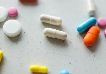 Assortment of white and brightly colored pills of different shapes and sizes scattered on a white tabletop